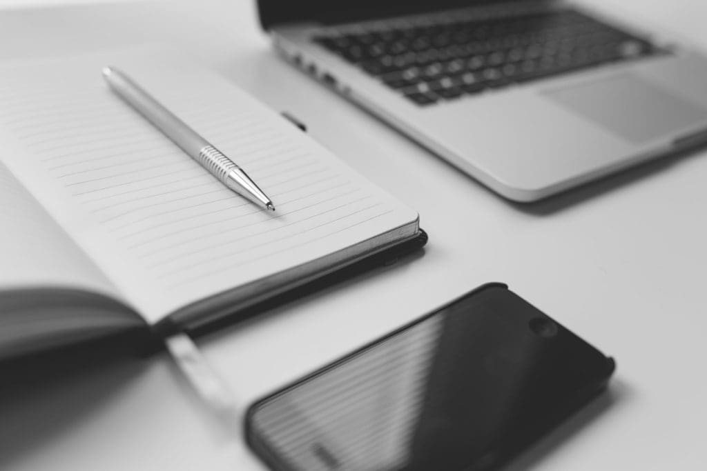 A notebook, pen, laptop and phone on a clean desk